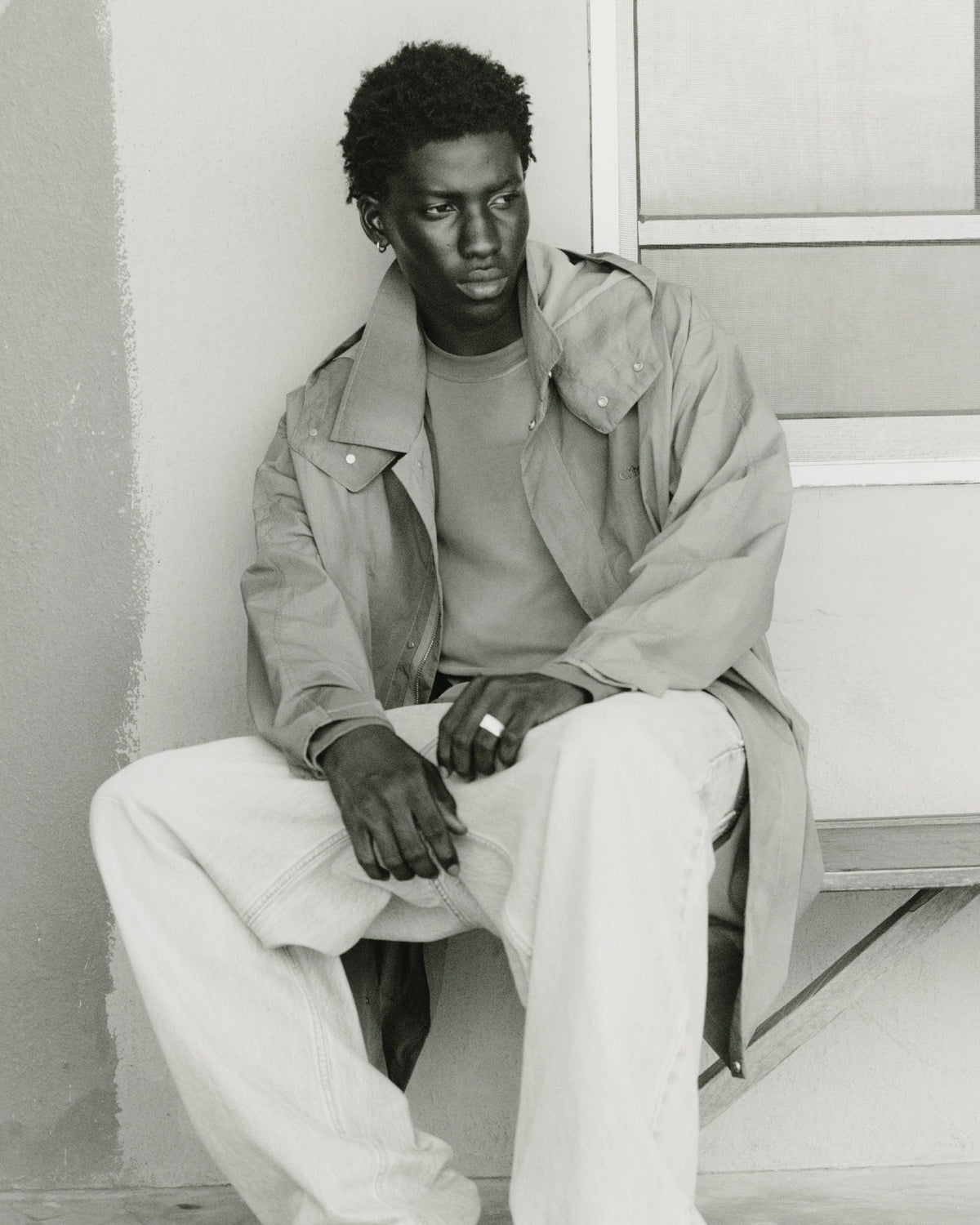 Arte Antwerp Automne-Hiver 2026 : homme assis en trench et pantalon clair, photo noir et blanc