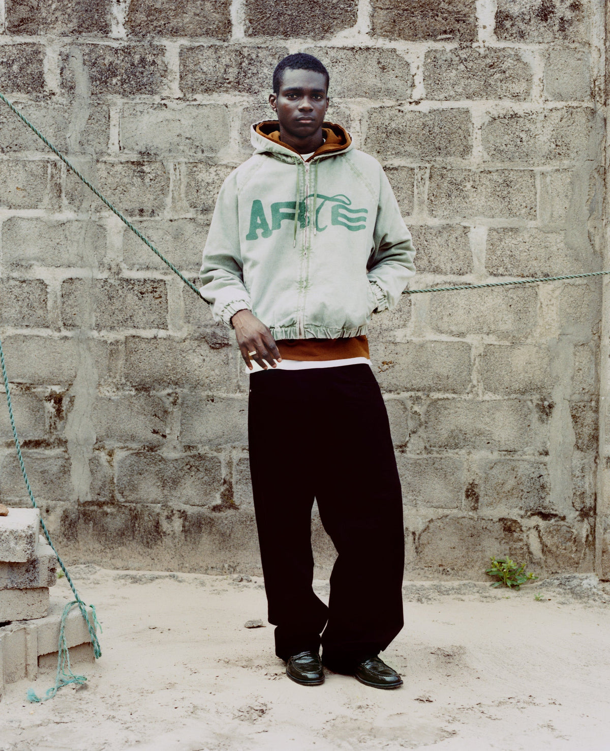 Campagne Arte Antwerp Automne-Hiver 2026 à Lagos — hoodie vert clair marqué Arte devant un mur de parpaings