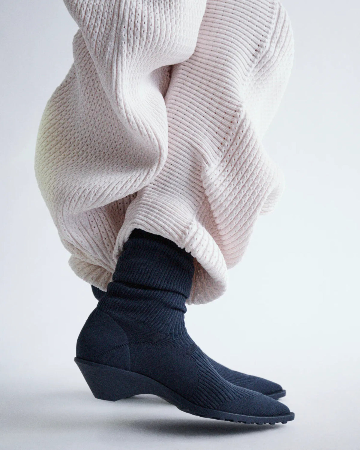 Camper × Issey Miyake Anna — bottine en maille noire portée sous un pantalon plissé