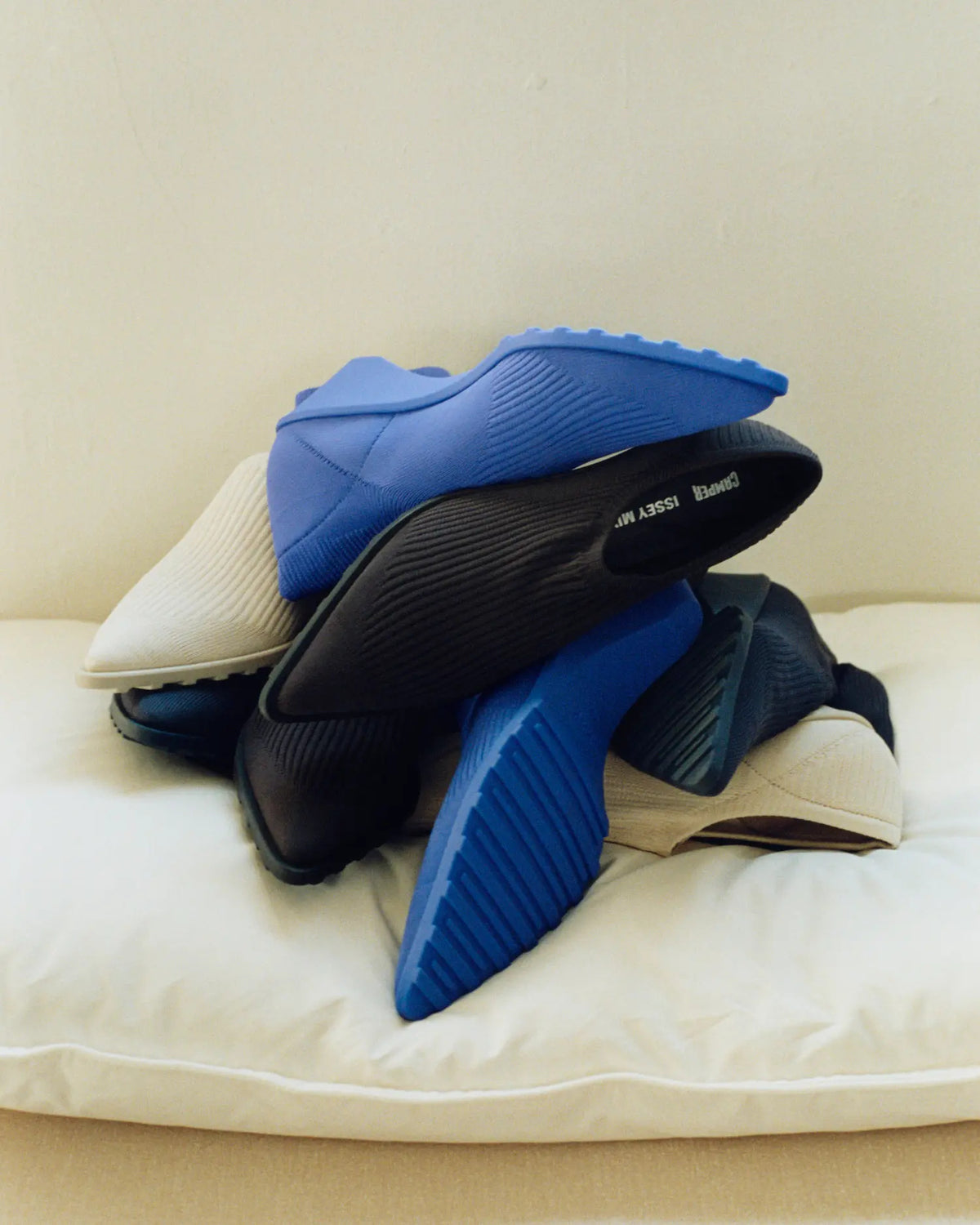 Camper × Issey Miyake Anna — bottines noires et bleues empilées sur un coussin, campagne