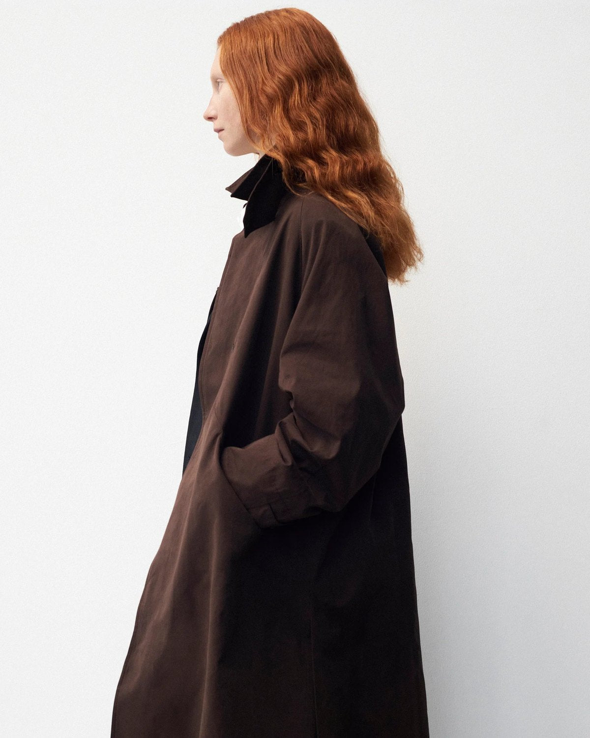Lookbook YMC AW26, femme de profil en long manteau brun