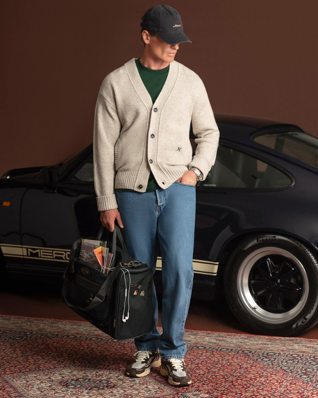 Campagne Mercer Automne-Hiver 2026 — homme en cardigan et jean devant une voiture noire, Re-Run Vintage Brown